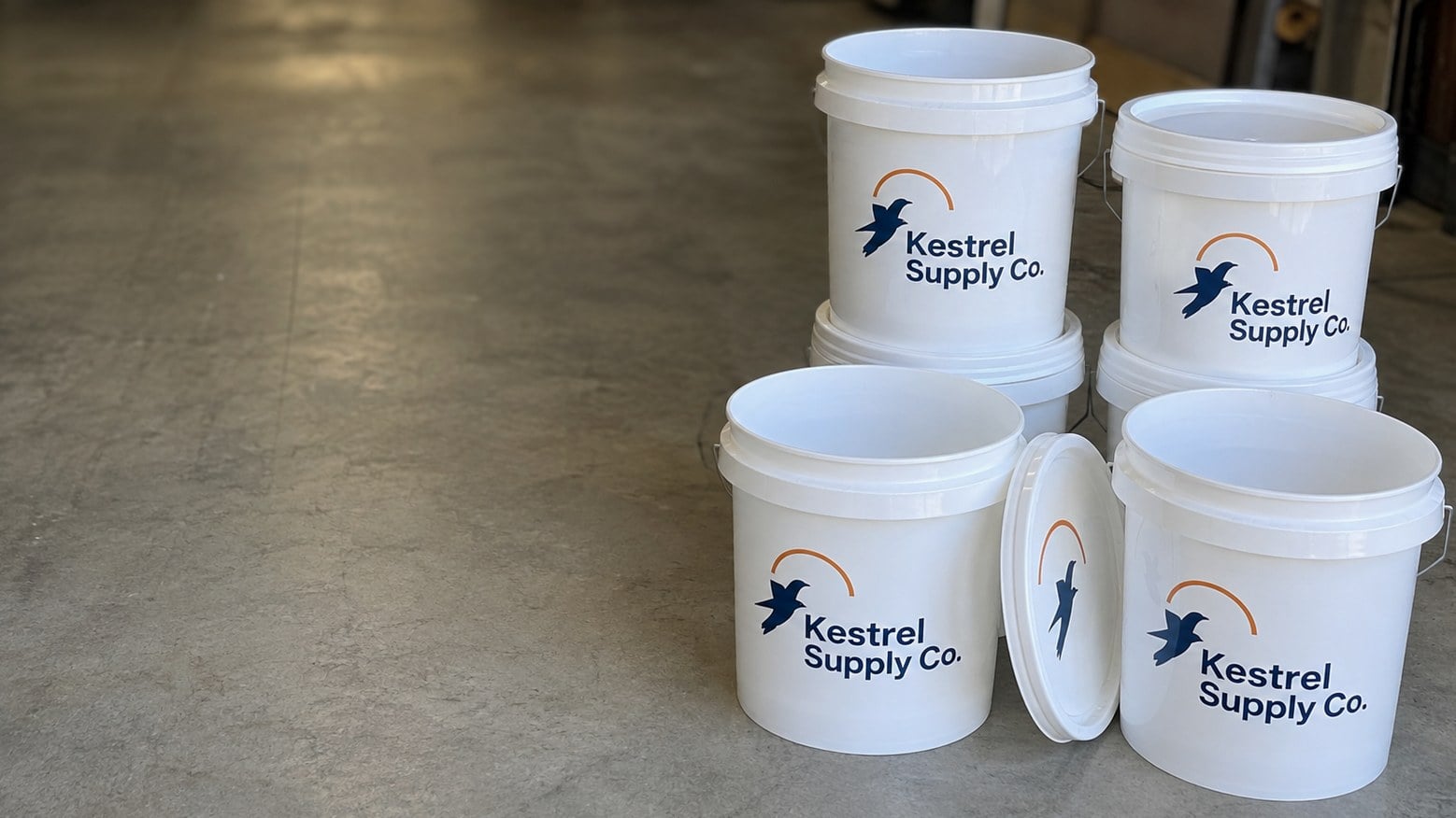 Custom printed 5 gallon buckets with a logo stacked on a workshop floor